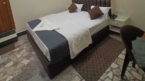 A hotel room with a bed, a nightstand, a chair, an air conditioning unit, and a ceiling fan.