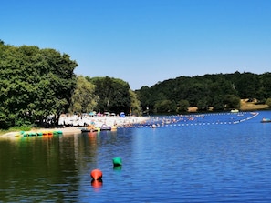 Una zona a la vora d'un llac, amb barques, una platja de sorra i arbres densos.