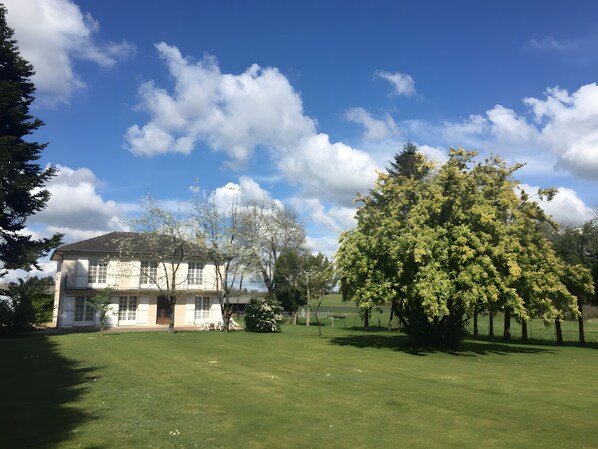 A two-story building with a lawn in front, surrounded by trees and a clear sky. - Large Family Home with Balcony, Garden & Lake Access near Périgord (Sauvagnac)