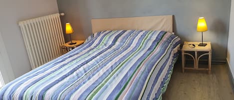 Una cama con colcha a rayas, dos lámparas de noche, una mesita de noche de madera y un radiador.