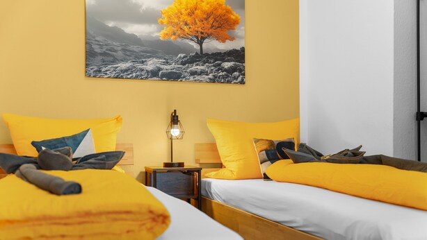 A hotel room with two beds, a nightstand with a lamp, and a painting of a tree on the wall. - Apartment 'Sun Design' with Balcony and Wi-Fi (Wuppertal)