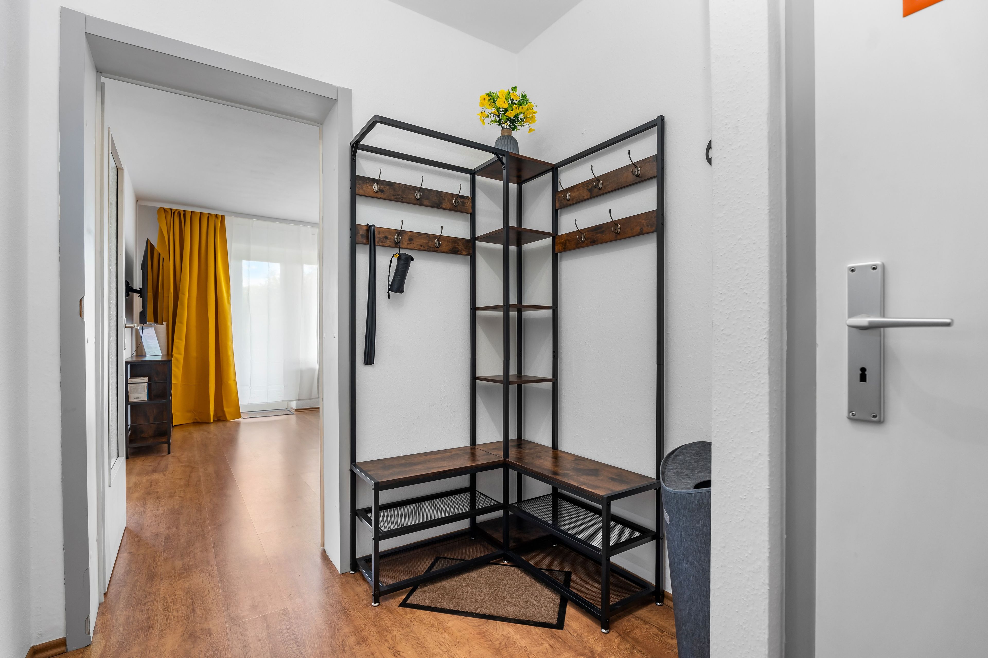 Ein Eckzimmer mit einem Metallregal, einer Tür und einem mit Vorhängen versehenen Fenster.