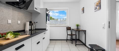 Une cuisine de taille réduite avec une fenêtre, une petite table avec une chaise et une poubelle.