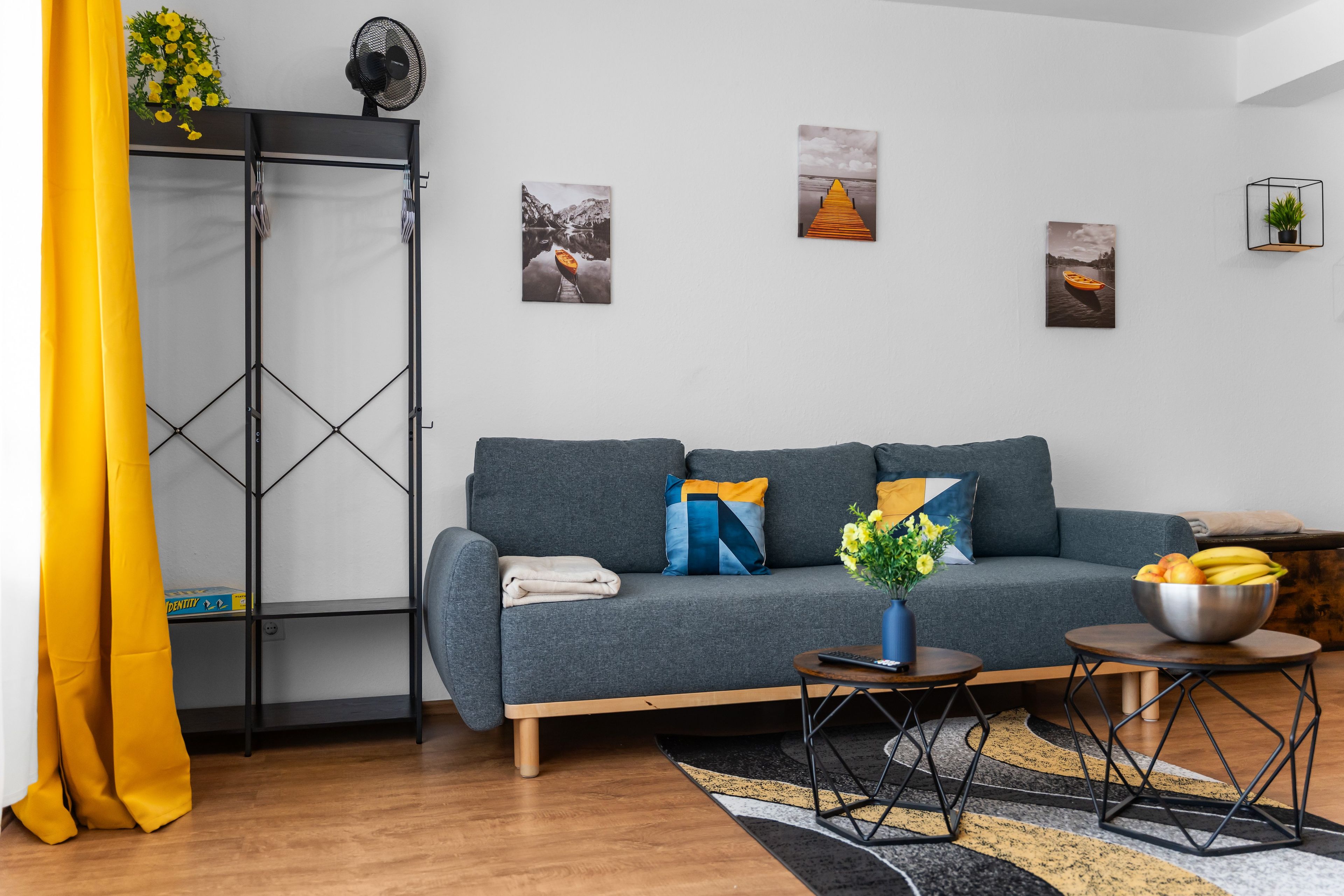 Ein modernes Wohnzimmer mit einem grauen Sofa, einem schwarzen Metallregal und Holzboden.