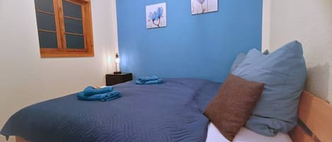 Une chambre à coucher comprenant un lit, une table de chevet, une lampe et deux tableaux accrochés au mur.
