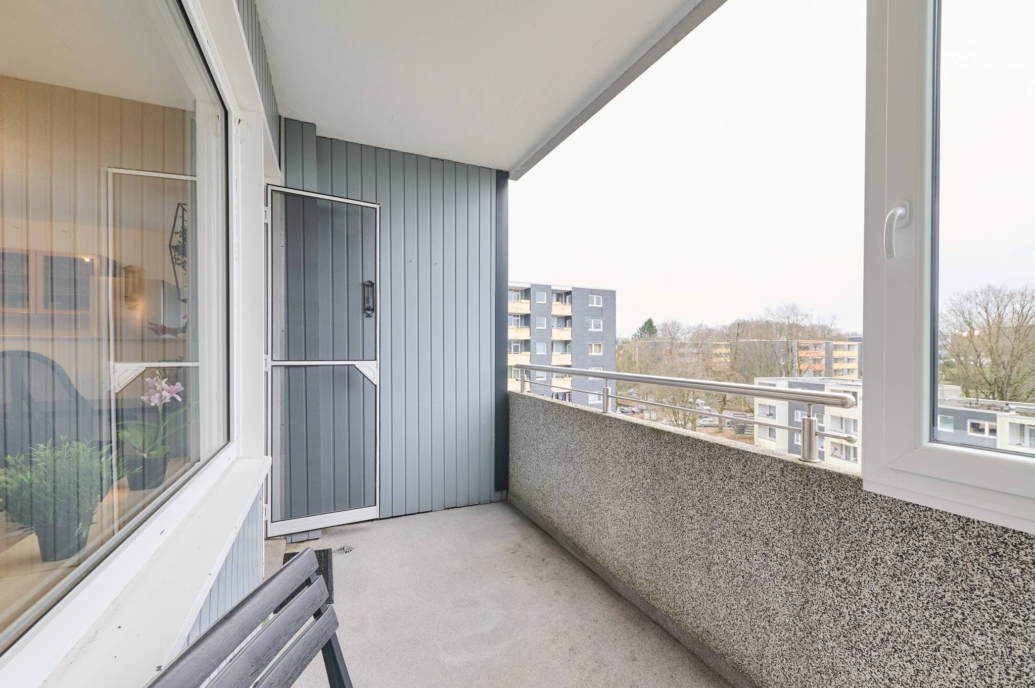 Ein Balkon mit Blick auf Gebäude, eine Tür und ein Fenster mit Pflanzen.