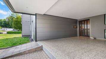 Un edificio moderno con un patio cubierto, entrada por puerta de vidrio y espacio exterior pavimentado.