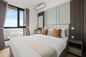 A modern hotel room with a large bed, a bedside table, a nightstand, a mirror, and an air conditioning unit. - Eron by Kozystay - Alam Sutera (Tangerang)