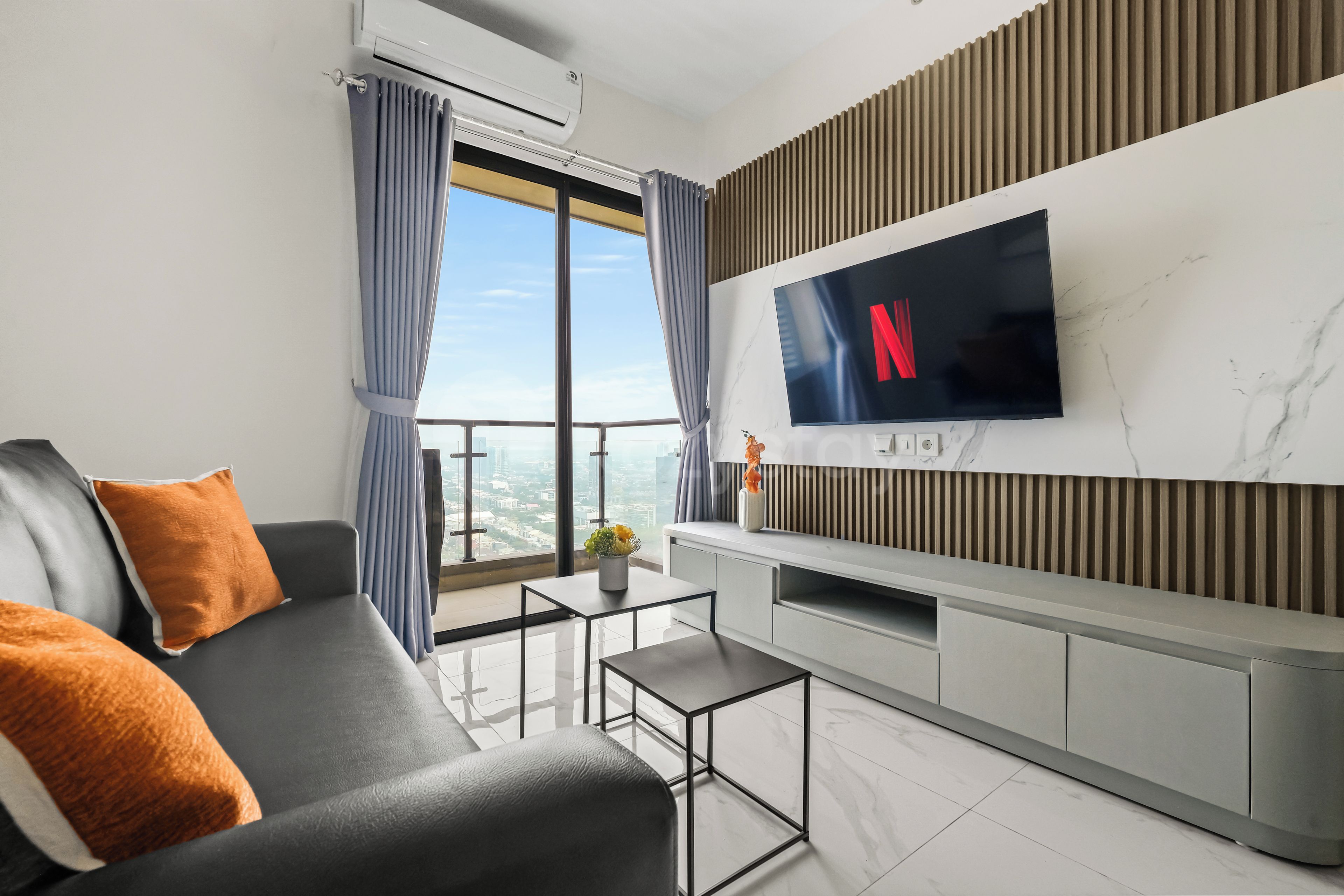 Een moderne woonkamer met een bank, een salontafel, een flatscreen televisie bevestigd aan een marmeren muur, en een stadszicht door grote ramen.