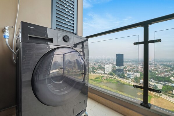 Een wasmachine met voorlaadklep in een kamer met een groot raam met uitzicht op een stadsgezicht.