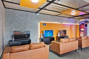 A modern lounge area with leather sofas, a flat-screen TV, and a gaming machine. - Eron by Kozystay - Alam Sutera (Tangerang)