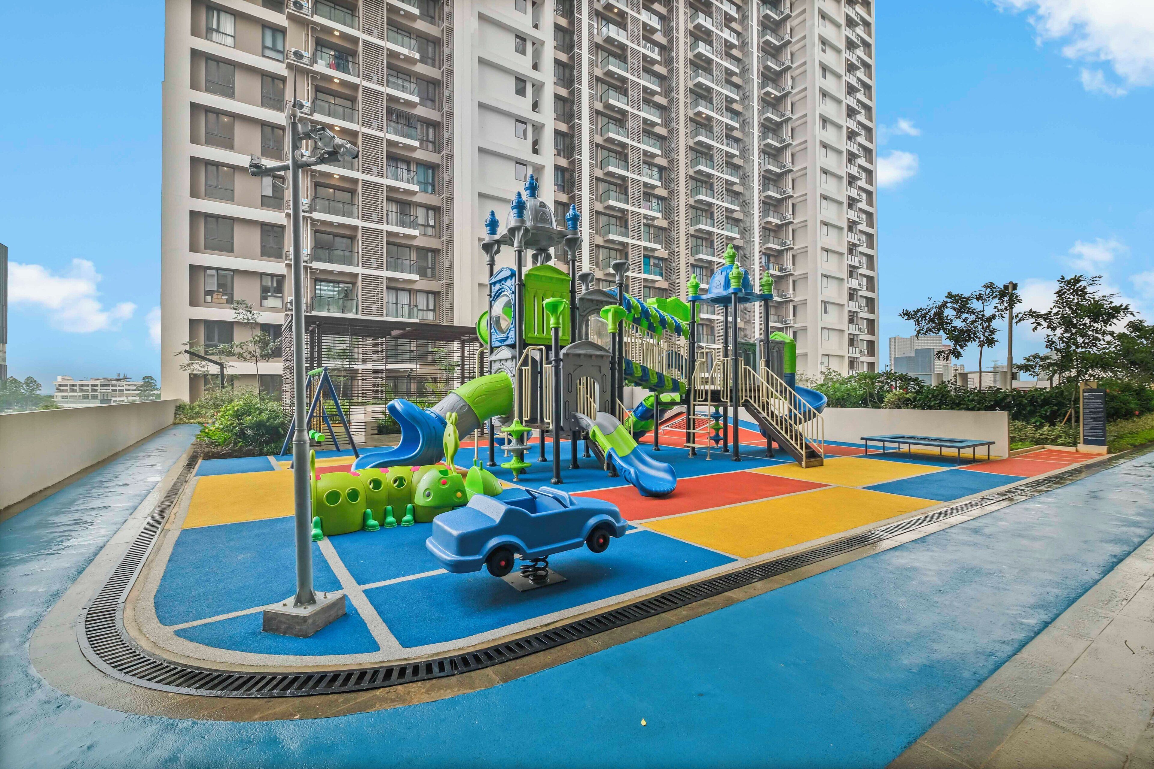 A playground with slides and climbing structures, surrounded by a high-rise residential building.