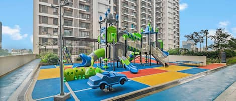 A playground with slides and climbing structures, surrounded by a high-rise residential building.