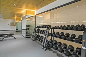 Een sportschool met halterrekken, banken en een spiegelwand.