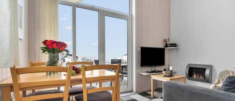 A modern living room with a dining area, a fireplace, and a large window offering a view.