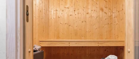 Una sauna de madera con un banco, un estante con piedras, y una toalla y una botella en el suelo.