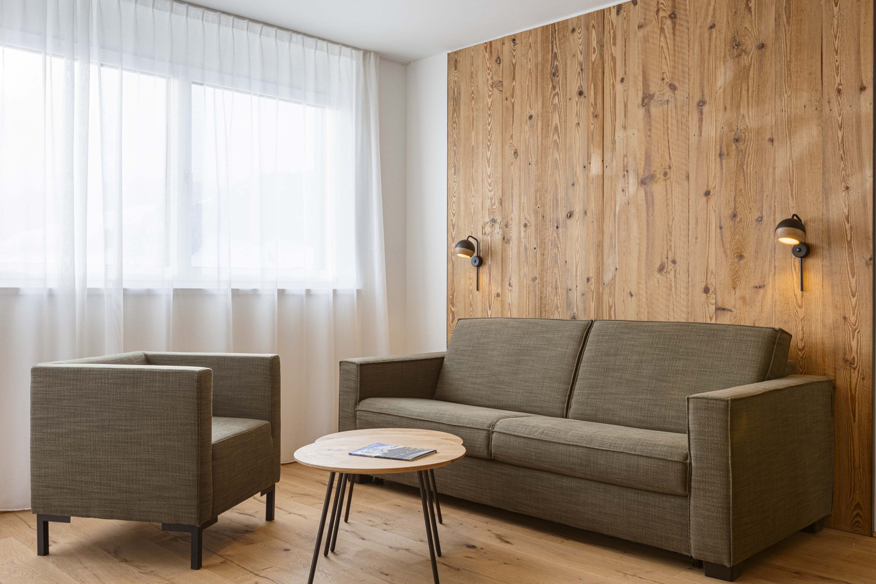 A modern living room with a wooden accent wall, a sofa, two armchairs, and a small round table.