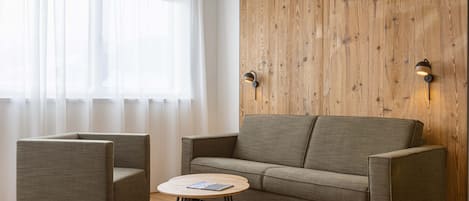 A modern living room with a wooden accent wall, a sofa, two armchairs, and a small round table.