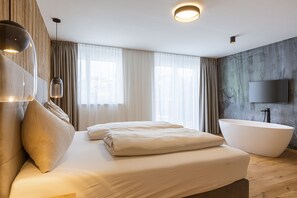 A modern bedroom with a large bed, a bathtub, and a TV mounted on the wall. - Ofs_e_superior Mh_2sz_m.b._fis_7 (Fiss)