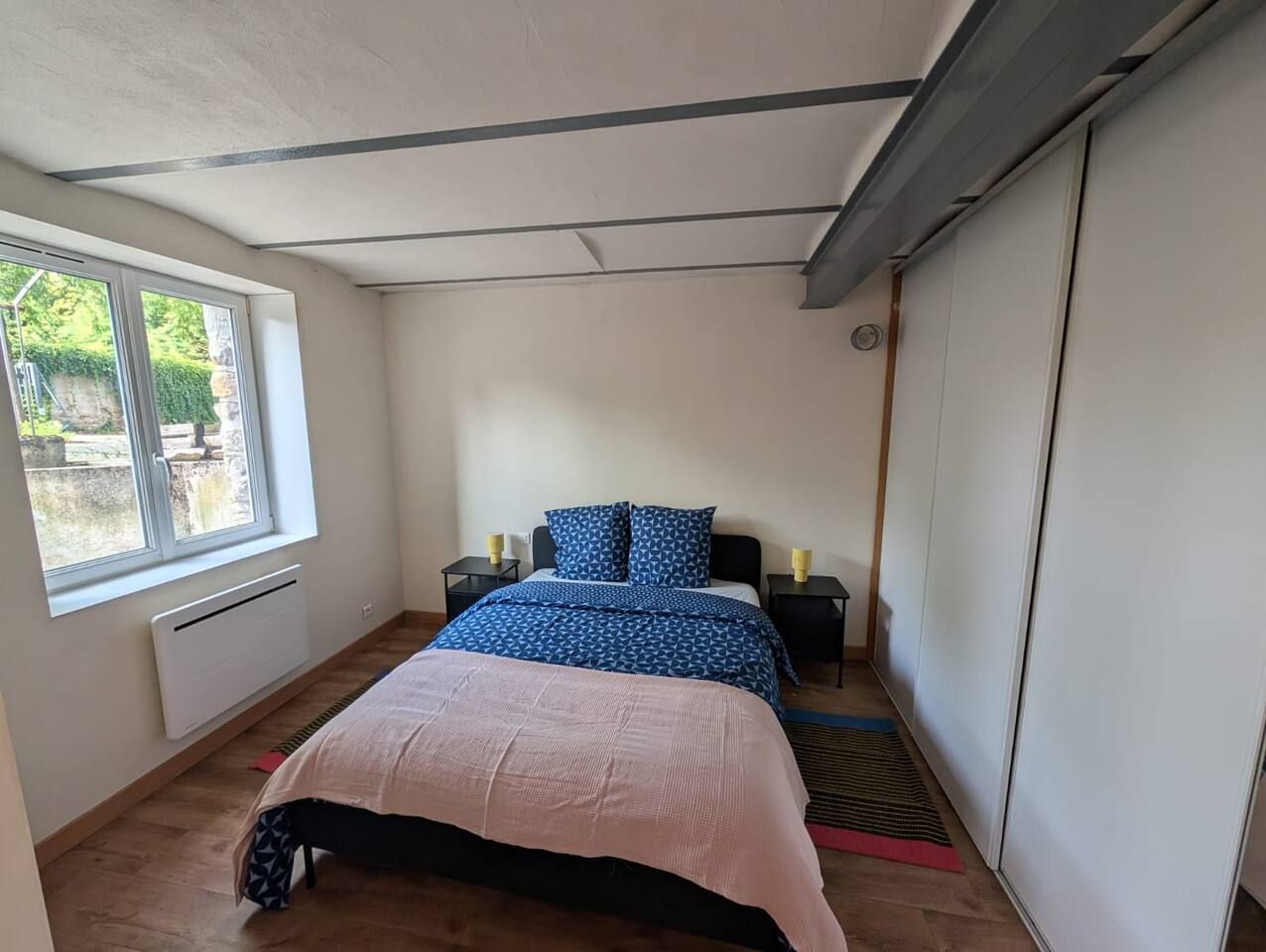Ein Schlafzimmer mit einem Bett, Nachttischen, einem Heizkörper, einem Fenster und einem Kleiderschrank.
