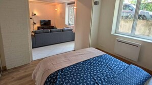 Ein Schlafzimmer mit Bett, Fenster und Blick auf einen Wohnbereich mit Sofa und Fernseher.