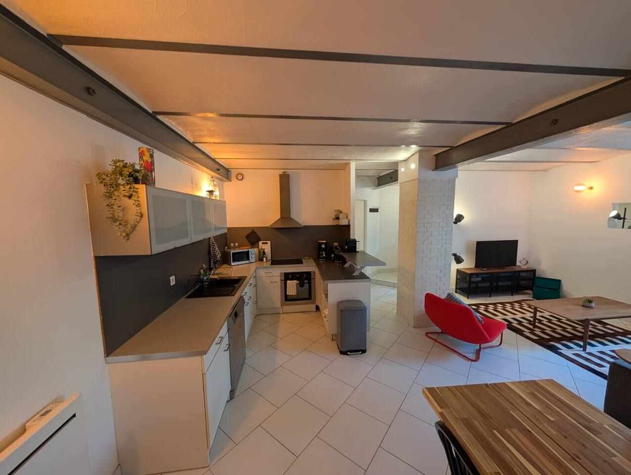 Eine moderne Küche mit einer zentralen Kochinsel, ein Essbereich mit einem roten Stuhl und ein Fernseher im Wohnzimmer.