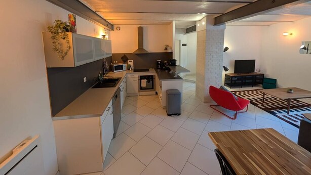 Eine moderne Küche mit einer zentralen Kochinsel, ein Essbereich mit einem roten Stuhl und ein Fernseher im Wohnzimmer.