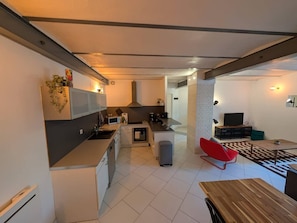 A modern kitchen with a central island, a dining area with a red chair, and a TV in the living room. - La Fabrique - Downtown Loft (Nancy)