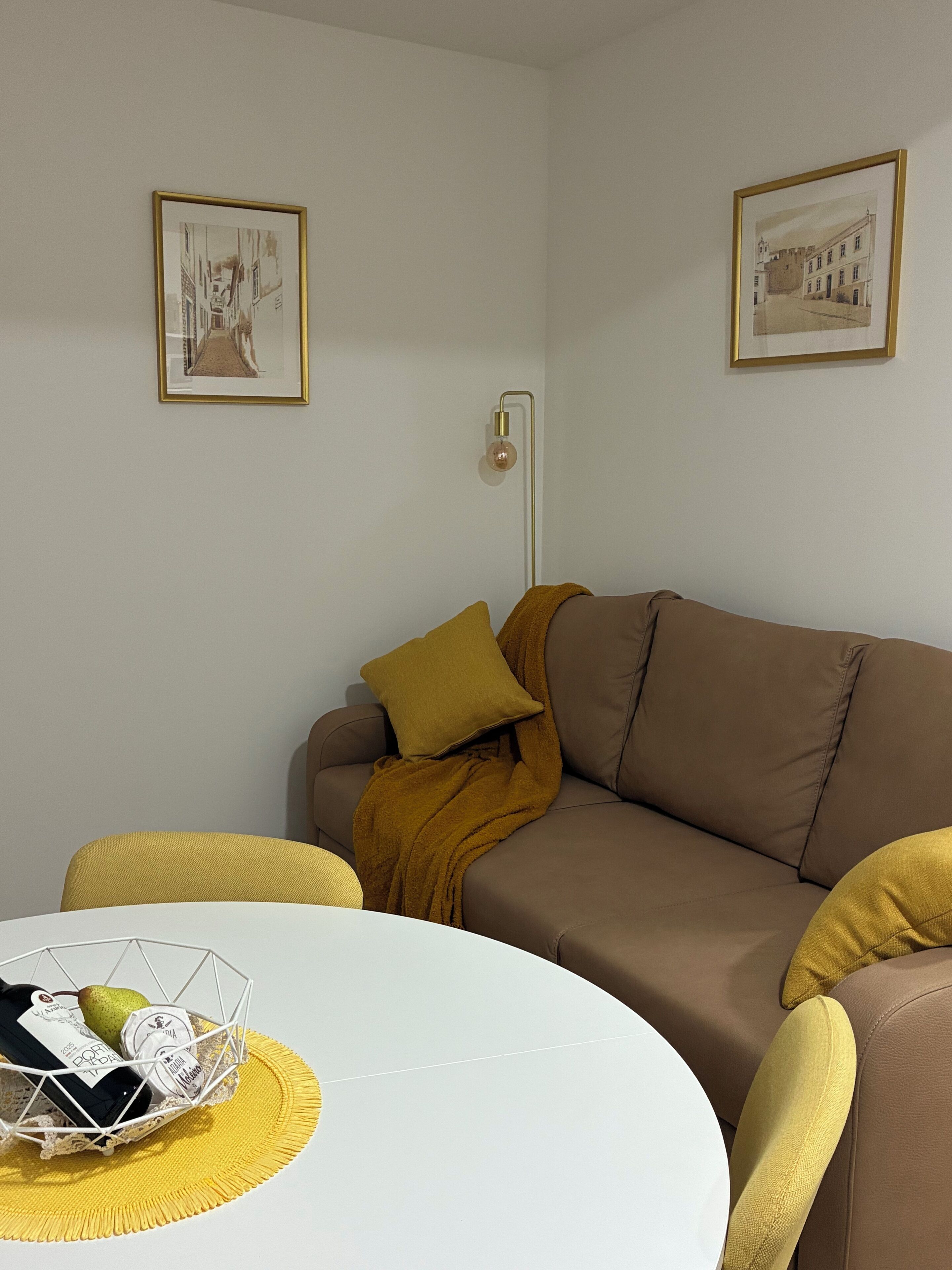 Una sala de estar con un sofá marrón, una mesa redonda blanca y dos cuadros en la pared.