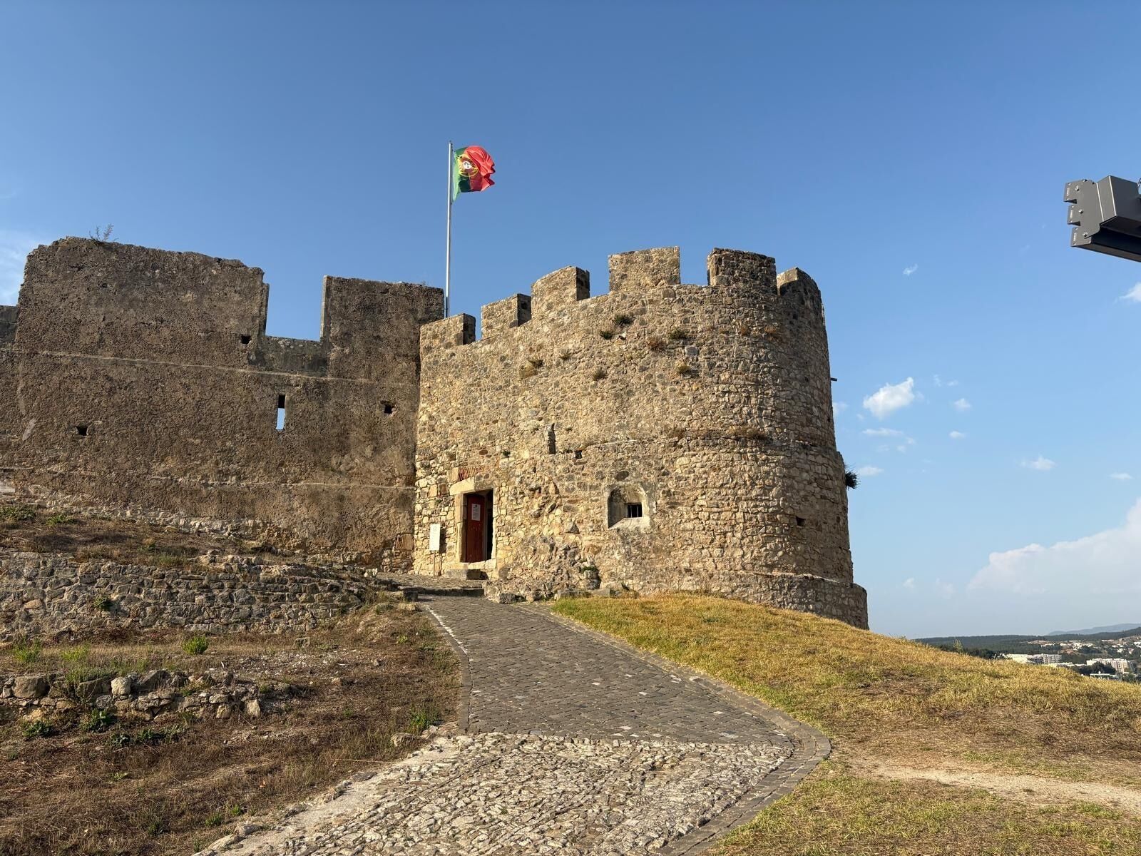 A historic stone castle with a flagpole, a central entrance, and a surrounding moat.