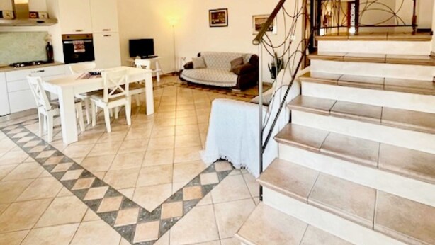 A spacious living area with a dining table, sofa, and staircase leading to an upper level. - Vrbo Property (Tortolì)