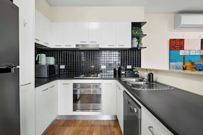 Eine moderne Küche mit weißen Schränken, einer schwarzen Fliesenrückwand, Edelstahlgeräten und Holzboden.