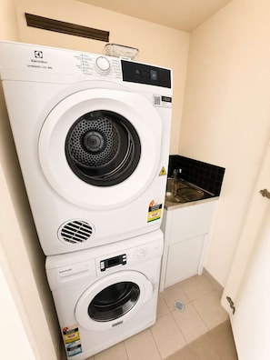 Eine gestapelte Waschmaschine und ein Trockner in einem kleinen Waschraum mit Spüle und Schrank.