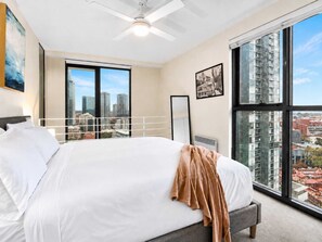 Ein Schlafzimmer mit einem großen Bett, einem Deckenventilator, einem Fenster mit Blick auf die Stadt und einem gerahmten Bild an der Wand.