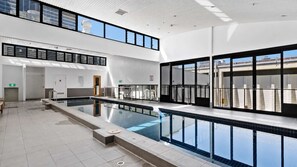 A modern indoor swimming pool with clear glass walls, a tiled floor, and a high ceiling with recessed lighting. - Gem by the mall, Pool, Gym, Parking, WIFI (Melbourne)