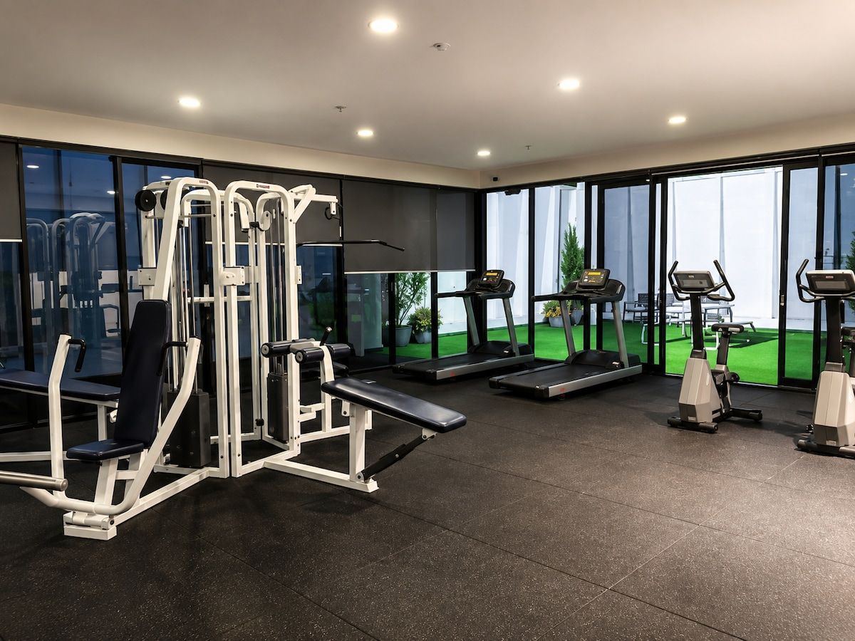 Een moderne sportschool met diverse fitnessapparaten, grote ramen en uitzicht op een groen buitengebied.