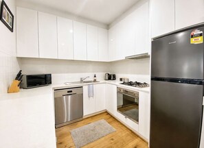 A compact kitchen with white cabinets, a stainless steel dishwasher, a built-in oven, a microwave, and a refrigerator. - Gem by the mall, Pool, Gym, Parking, WIFI (Melbourne)