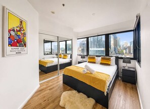 A modern hotel room with a city view, a large bed with yellow bedding, a mirror, and a framed artwork on the wall. - Gem by the mall, Pool, Gym, Parking, WIFI (Melbourne)