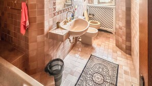 Une salle de bain équipée d’une baignoire, d’un lavabo et de toilettes, avec des murs carrelés et un tapis à motifs.