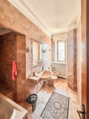 Ein Badezimmer mit Badewanne, Waschbecken und Toilette, mit gefliesten Wänden und einem gemusterten Teppich.