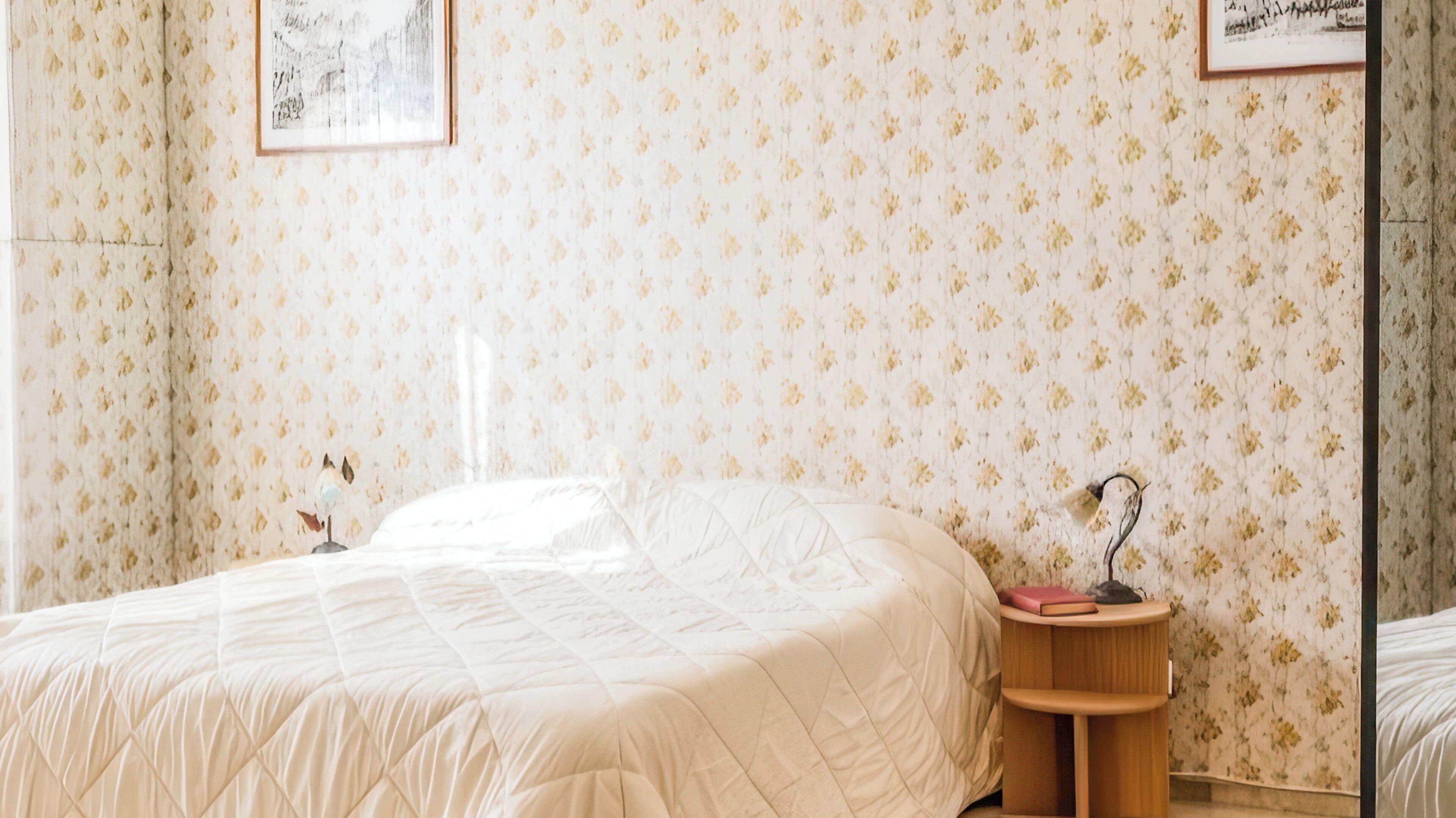 A bedroom with a bed, a bedside table, and a wall with floral wallpaper.