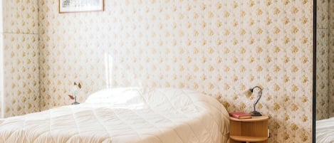 A bedroom with a bed, a bedside table, and a wall with floral wallpaper.