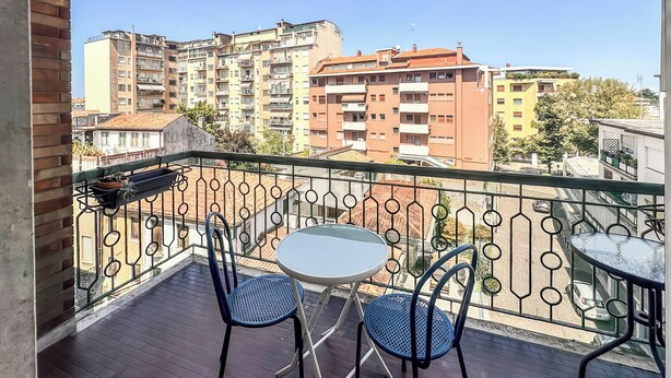Un balcon avec une table et deux chaises, donnant sur un quartier résidentiel composé d’immeubles à plusieurs étages.
