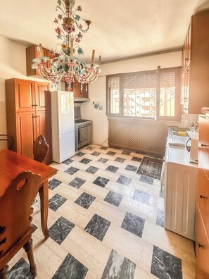 Eine Küche mit Fliesenboden, Holzschränken, einem Kühlschrank, einem Herd und einem Fenster mit Blick.