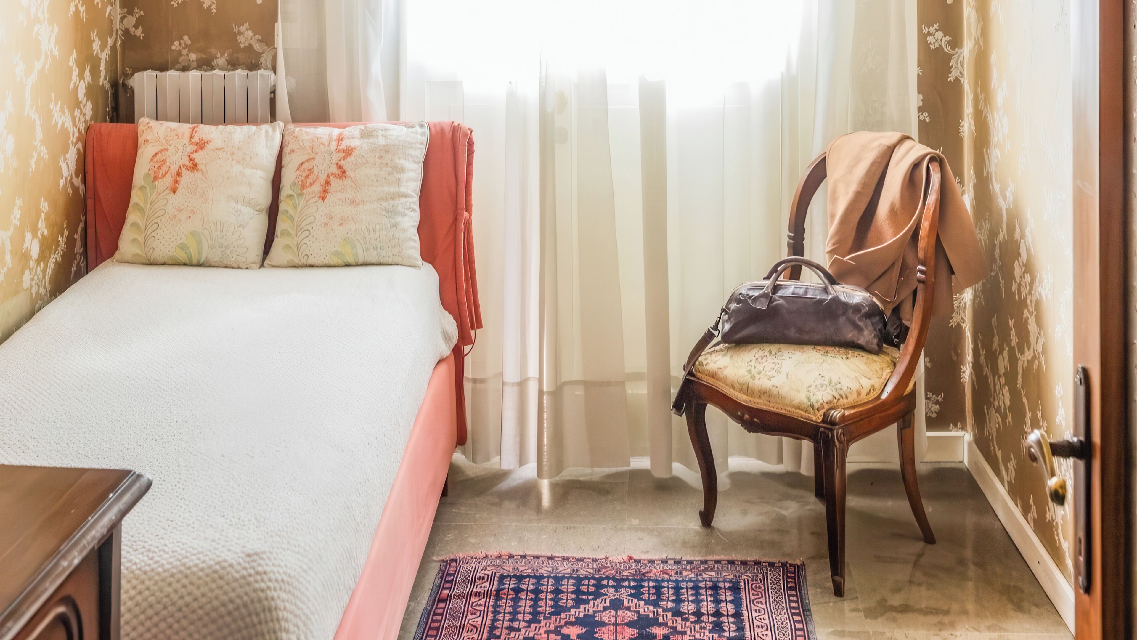 Ein Schlafzimmer mit einem Bett, einem Sessel, einem Teppich und einem Fenster mit Vorhängen.