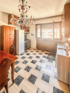 A kitchen with a tiled floor, wooden cabinets, a refrigerator, an oven, and a chandelier. - Civico 9 (Mestre)