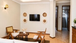 A living room with a sofa, chairs, a coffee table, a flat-screen TV, and decorative wall art. - The Valley Retreat (Arusha)