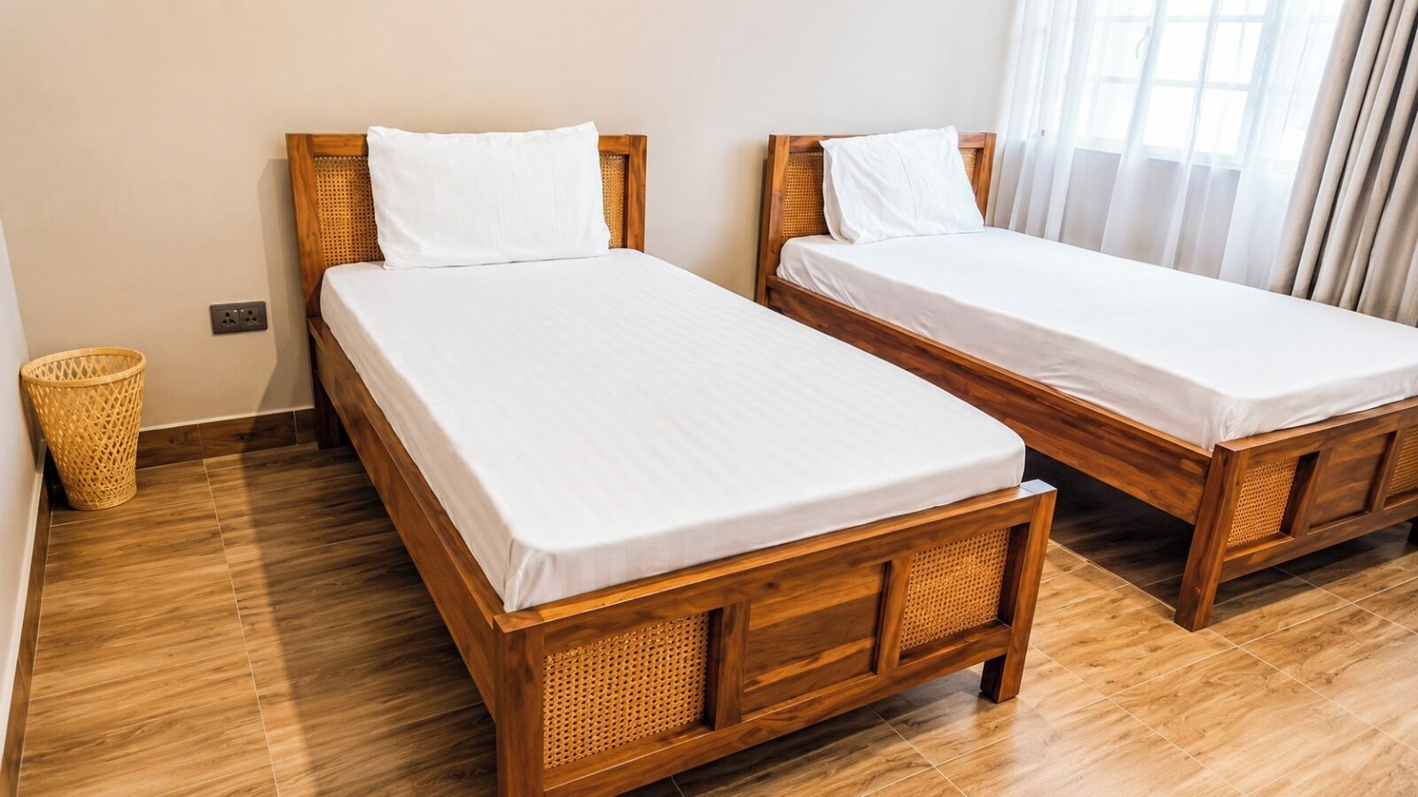 Una habitación con dos camas de madera, una cesta de mimbre y suelo de baldosas.