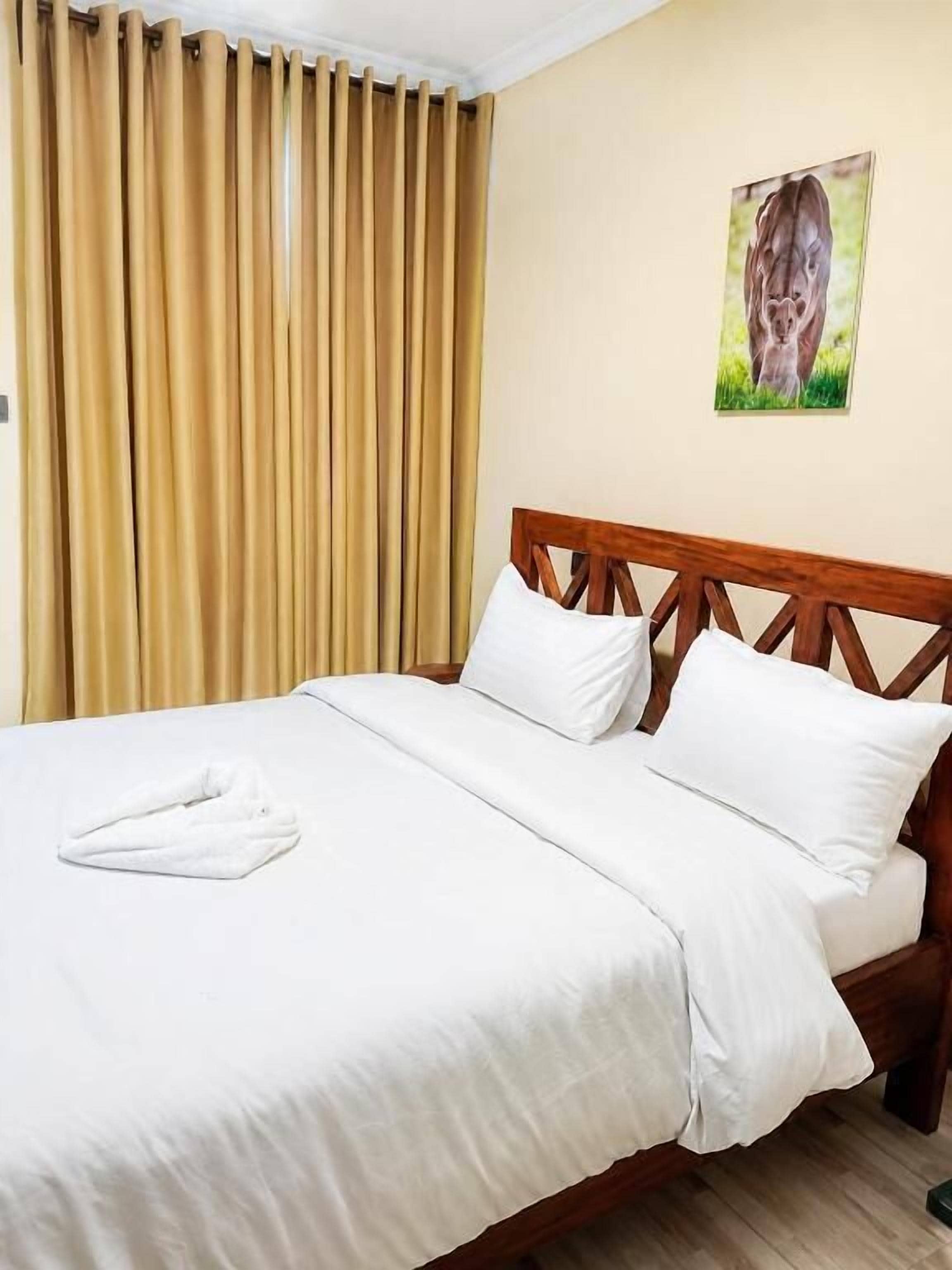 A hotel room with a bed, curtains, and a painting on the wall.
