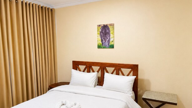 A hotel room with a bed, a wooden headboard, a small table, and a painting on the wall. - The Valley Retreat (Arusha)